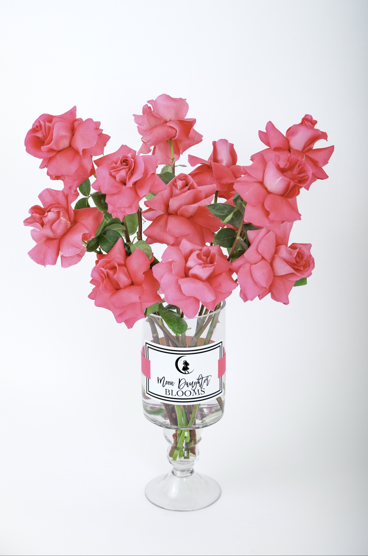 Flower Subscriptions — pink roses in a clear glass pedestal vase with a Moon Daughter Blooms logo label